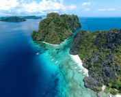 Aerial view of dramatic limestone karst cliffs, turquoise reefs and outrigger boats at the El Nido end of the Port Barton expedition, Palawan