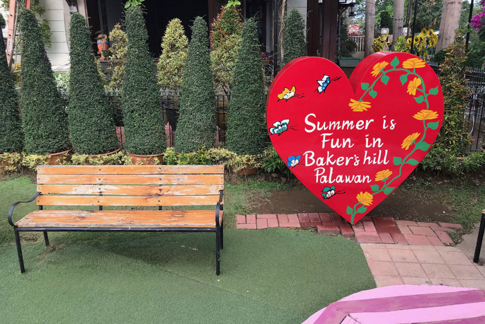 Baker's Hill welcome sign with red heart-shaped decoration surrounded by topiary trees and garden bench in Puerto Princesa, Palawan