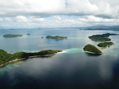 Aerial view of small green islands scattered across calm blue water under a soft cloudy sky, northern Palawan