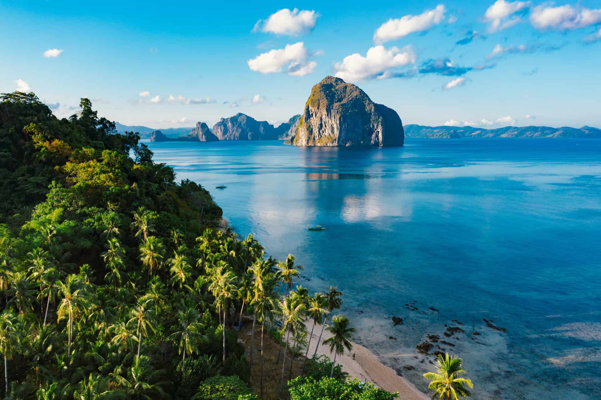 El Nido bay with karst island and palm-fringed coast at golden hour