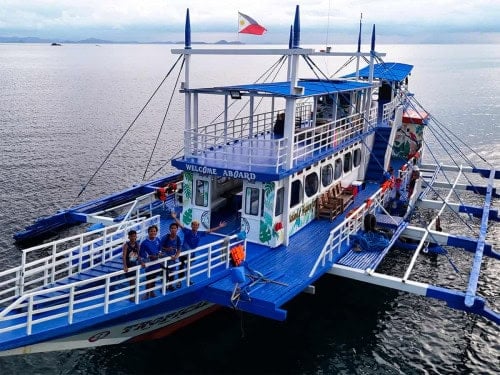Smiling crew on board the blue El Nido Paradise expedition boat with Welcome Aboard sign and Philippine flag